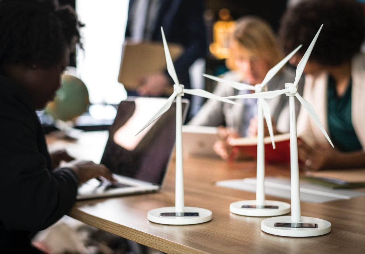 Three desktop solar powered model wind turbines demonstrating renewable energy while three women work on laptops in background